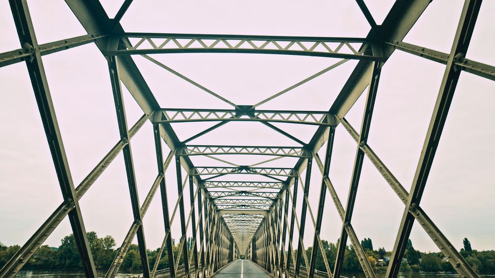Steel truss bridge structure stretches into the distance under a pale sky.