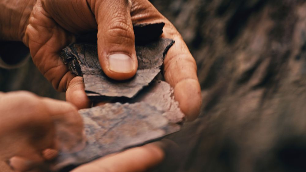 Craftsperson carefully smooths edges of a leather material using basic hand tools.