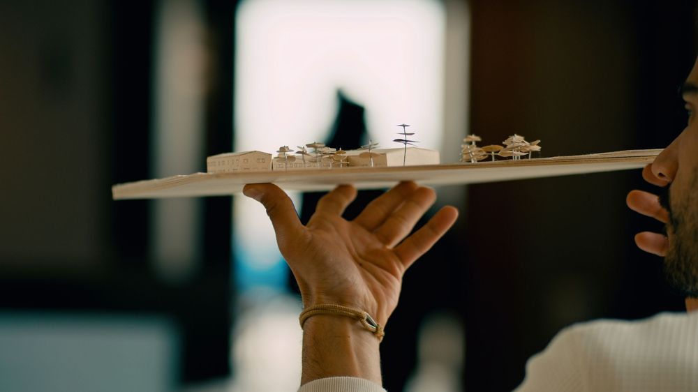 Hand holding up a white dish plate balancing a black cat figurine on top against a blurry background.