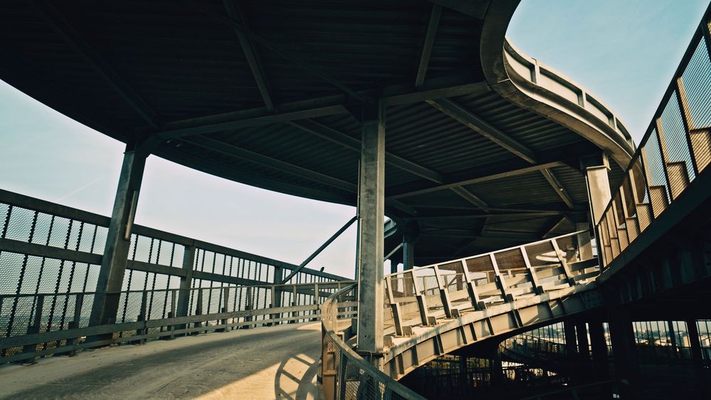 Dynamic panoramic view of an industrial bridge structure with geometric shapes against a bright blue sky.