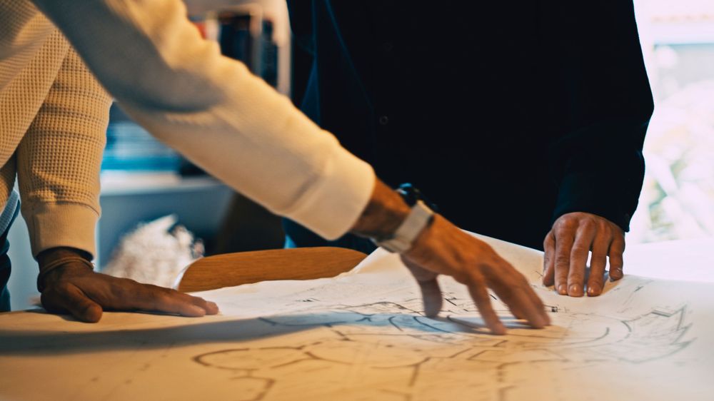Close-up view of hands collaborating on architectural blueprints and drawings on a desk during a planning meeting.