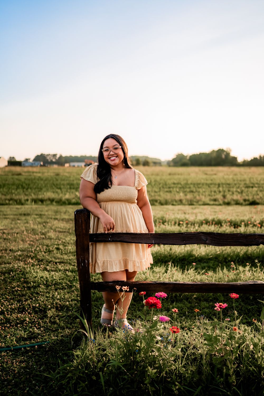 Pink flowers bloom near a rustic wooden fence in a golden sunset-lit field during summer.