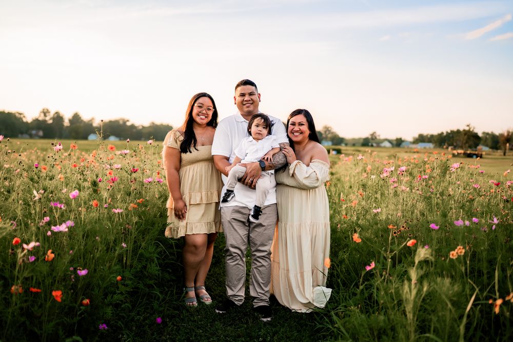 A family enjoys quality time together while sitting in a flower-filled field during golden hour.