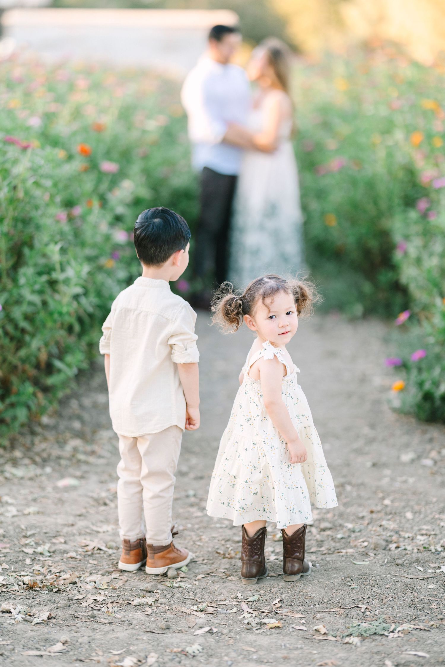 Children in coordinating outfits walking along a garden path during sunset.