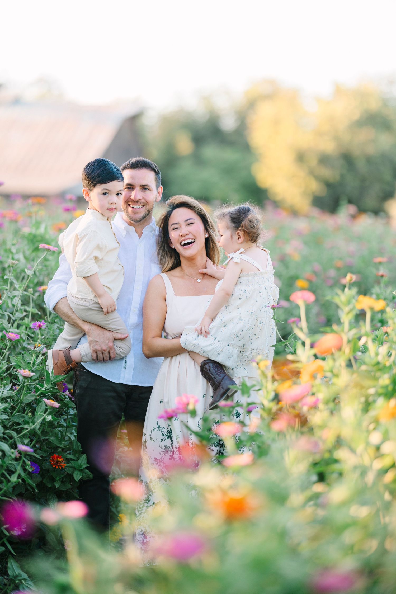 Family laughs together surrounded by colorful summer flowers in a garden path.
