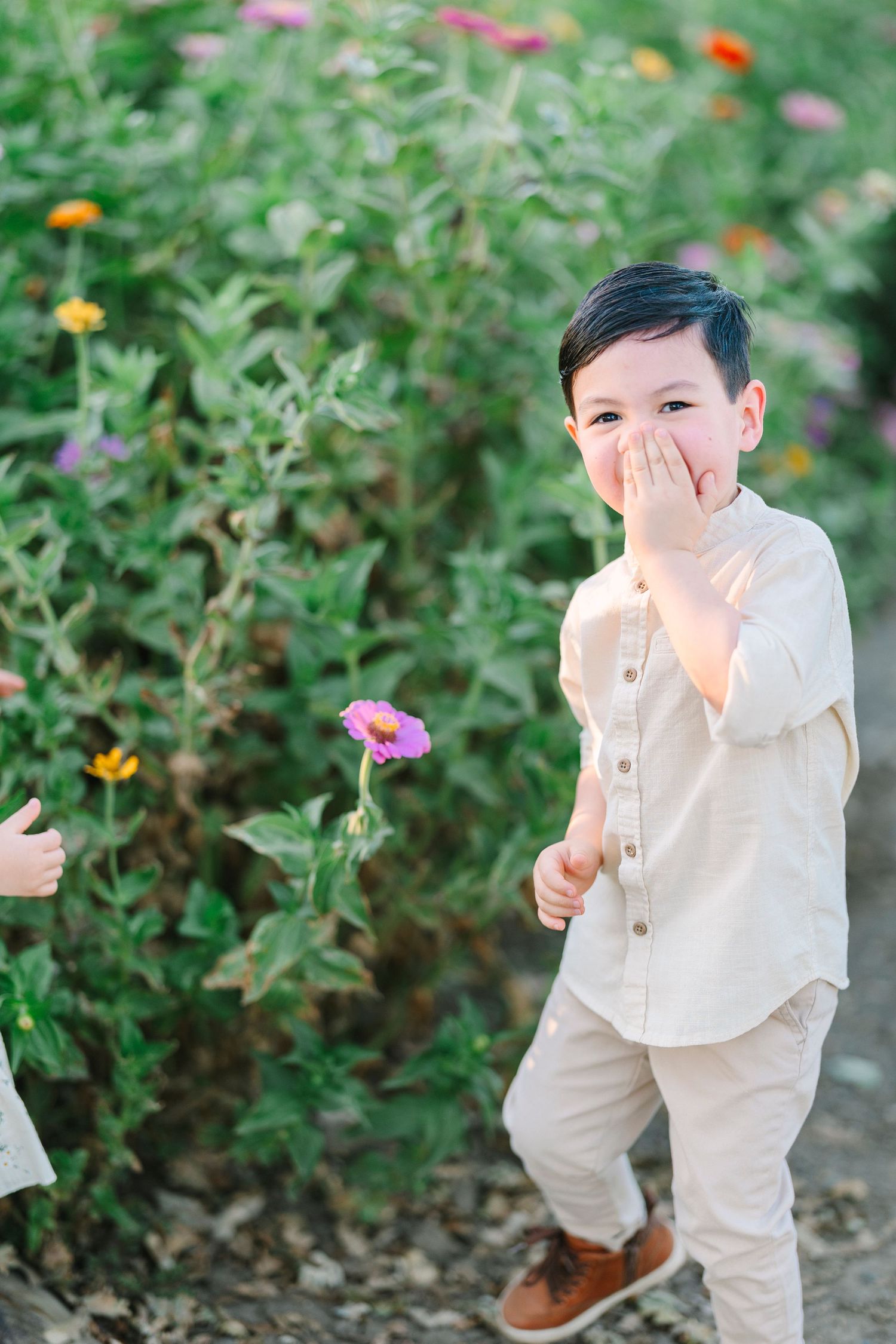 Child in white clothing plays hide and seek among flowering garden plants.