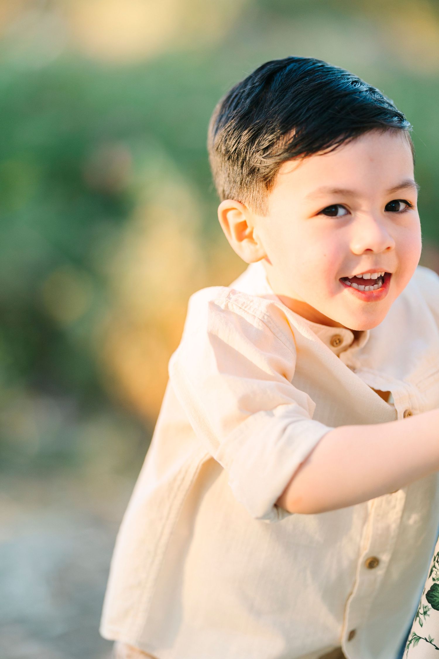 Child in cream colored outfit plays and smiles outdoors in natural lighting.
