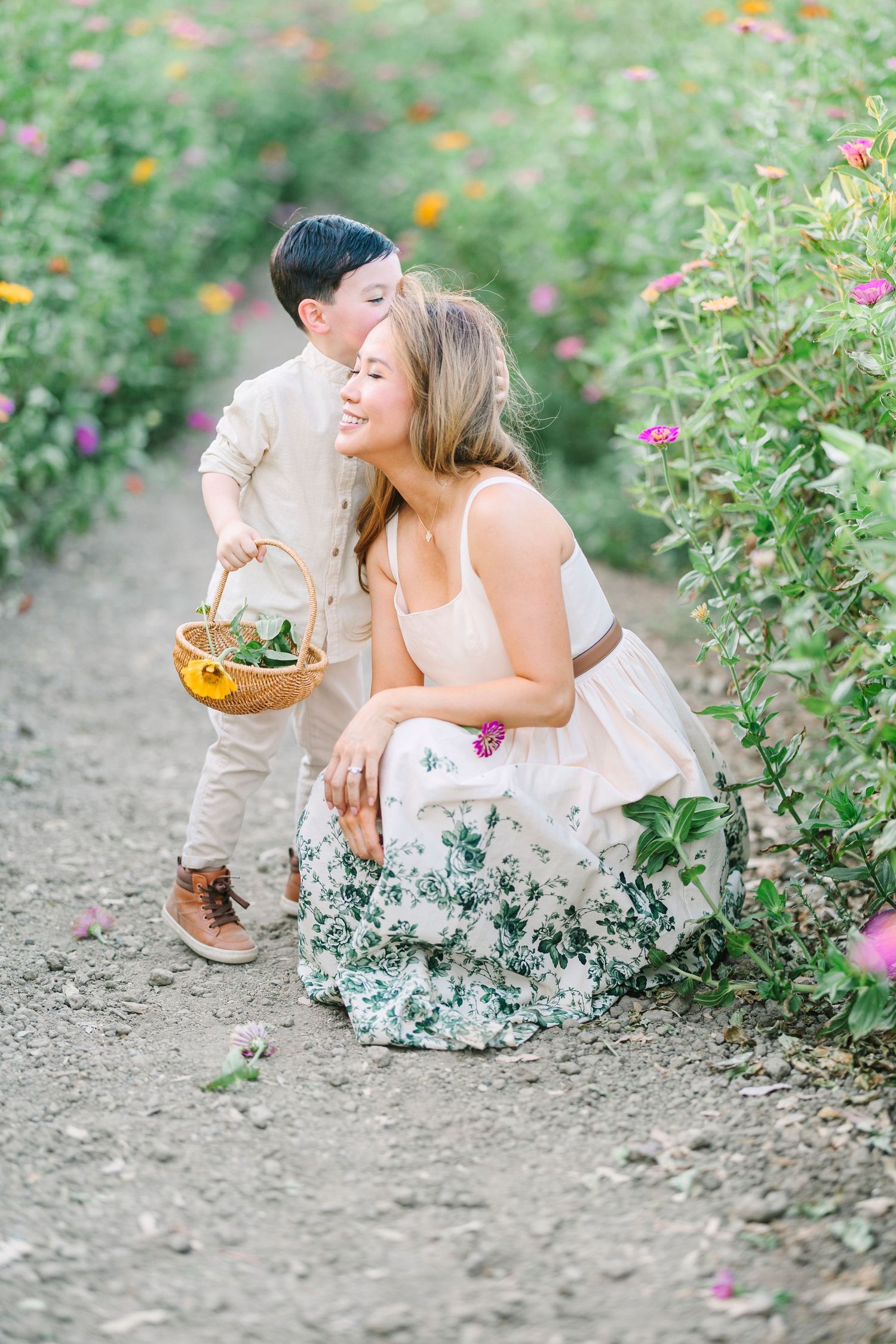 Parent and child interact playfully on a dirt path between flowering plants.