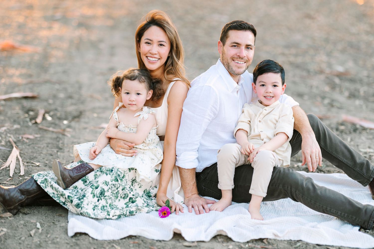 A family of four poses together on a blanket for a casual outdoor portrait.