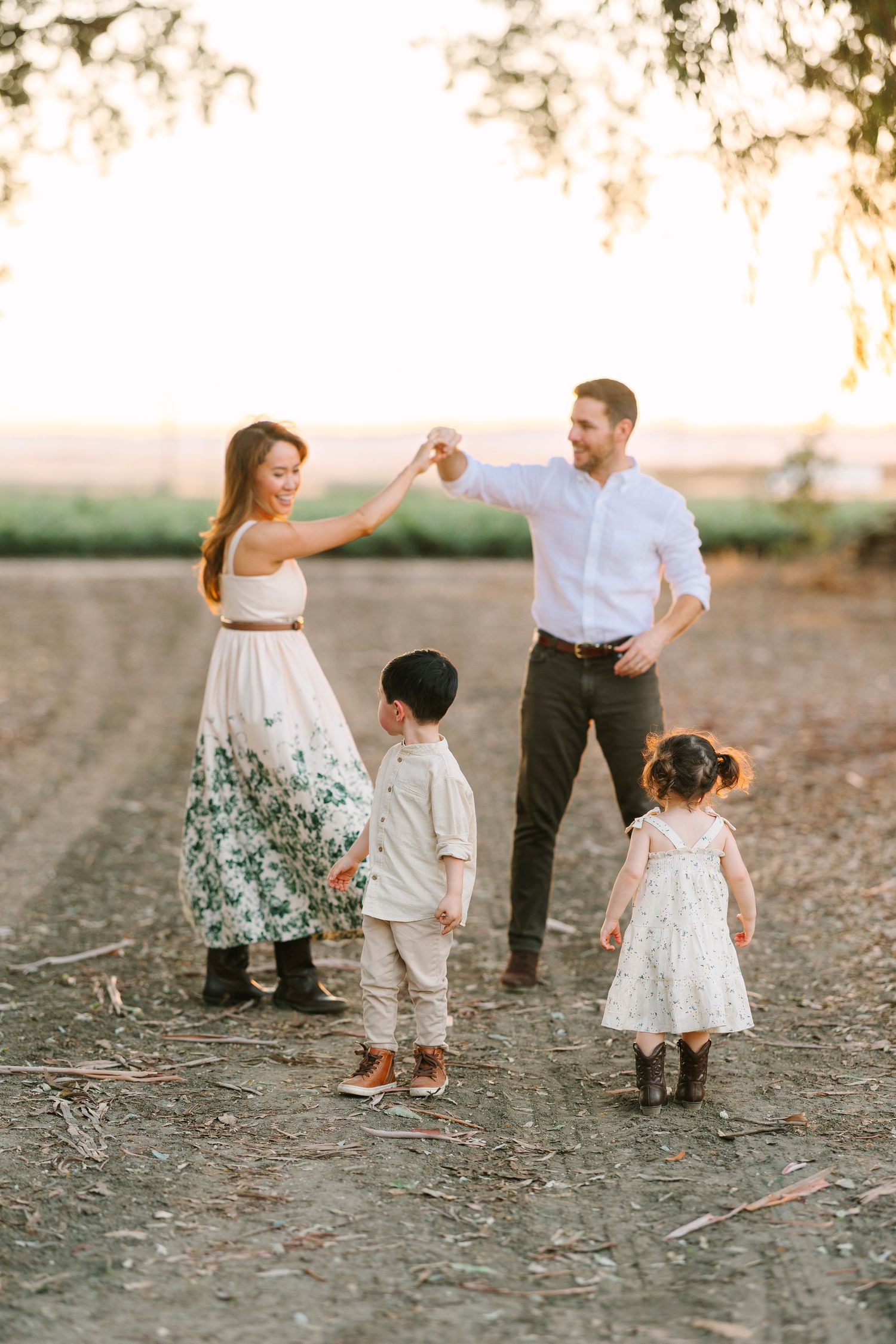 A family shares a playful dance moment together on a dirt path at sunset.