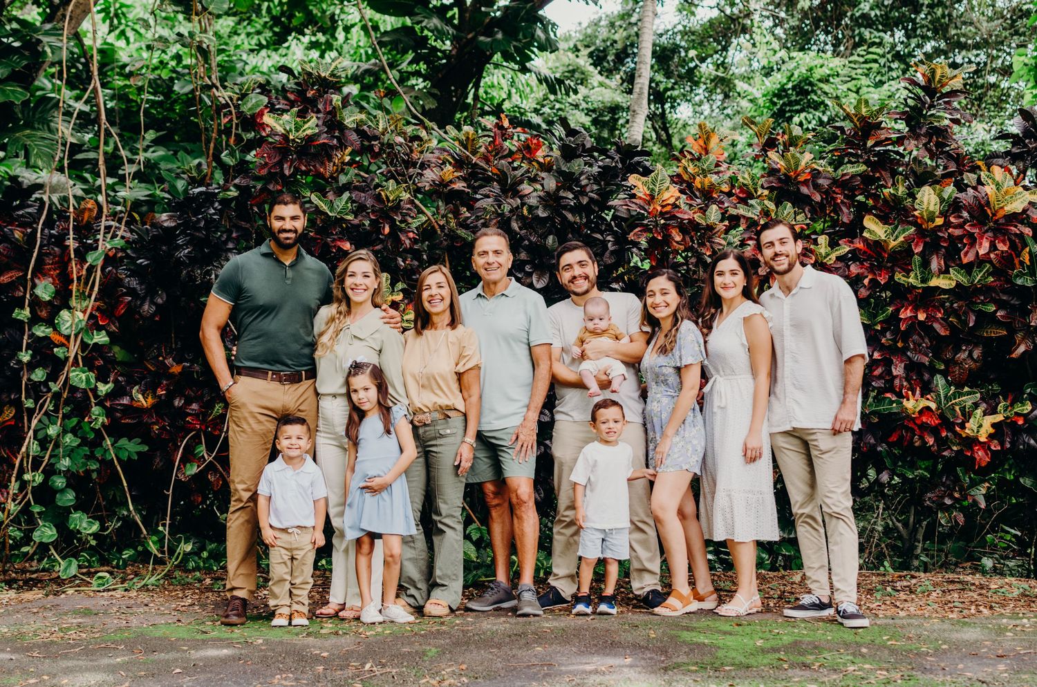 Extended family group poses together in coordinated white and neutral outfits against tropical background.
