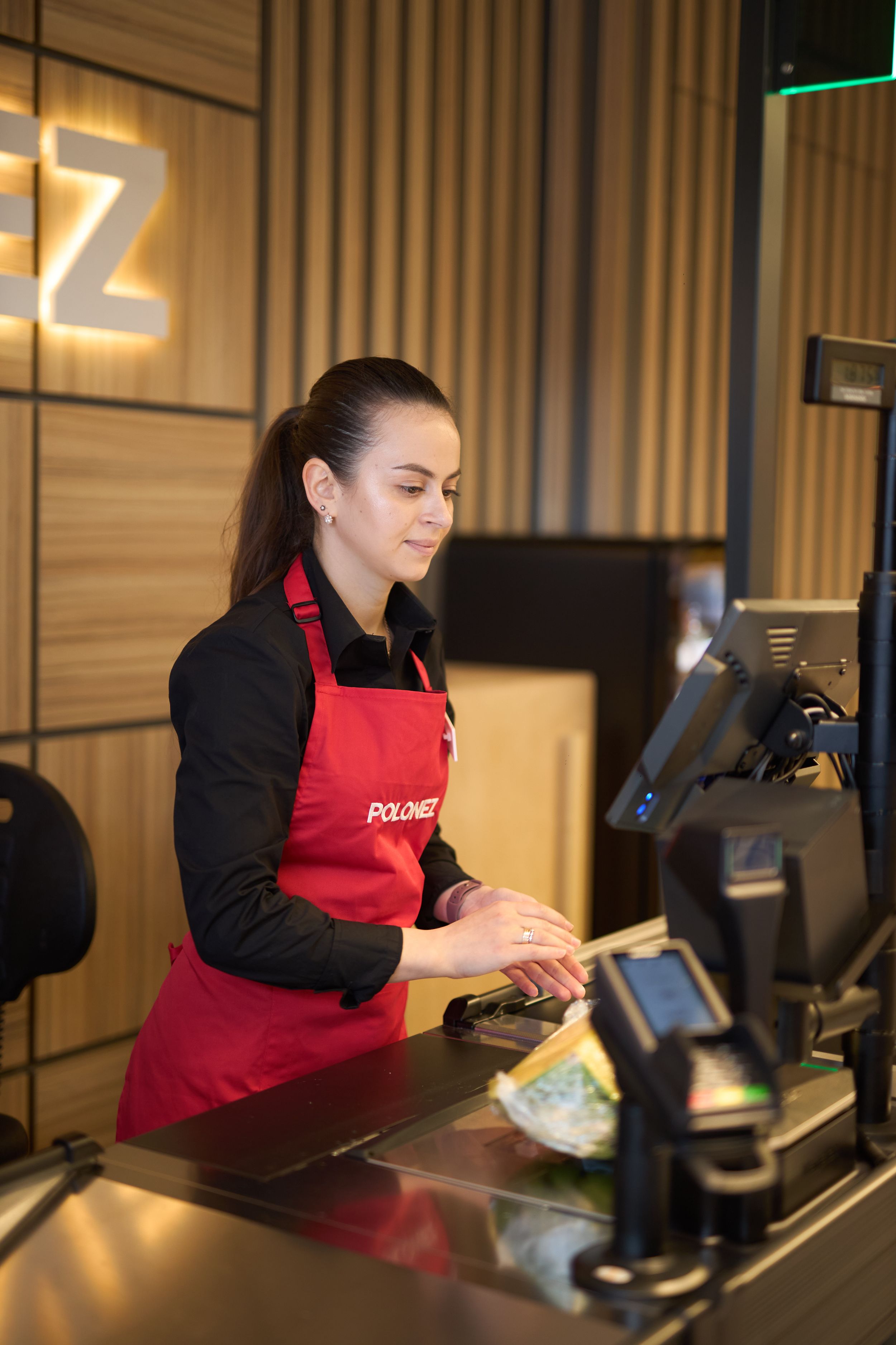 Staff member in red apron operates point of sale system at retail counter.