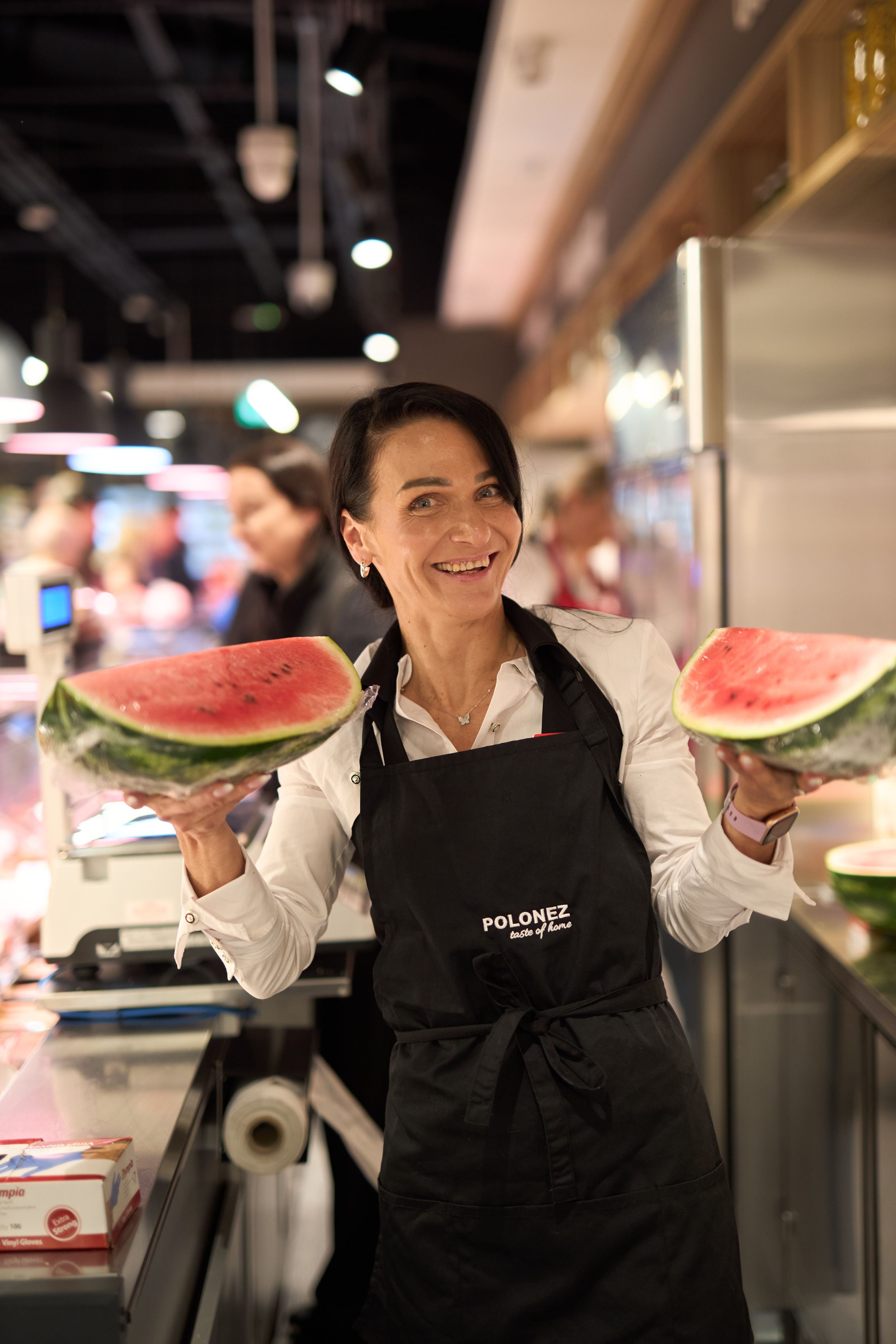 Employee in black apron displays fresh watermelon slices in retail setting.