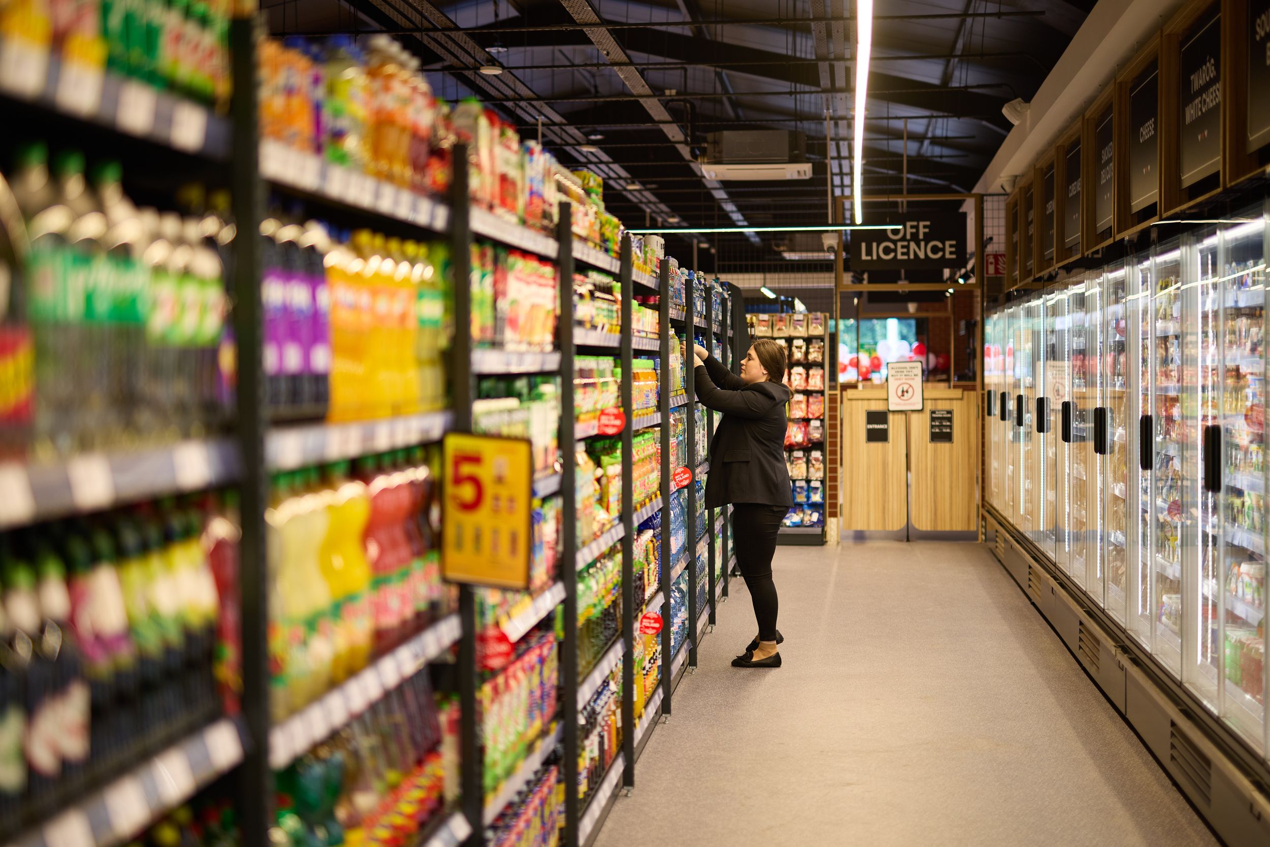 Long view of supermarket aisle with refrigerated cases and colorful product displays.