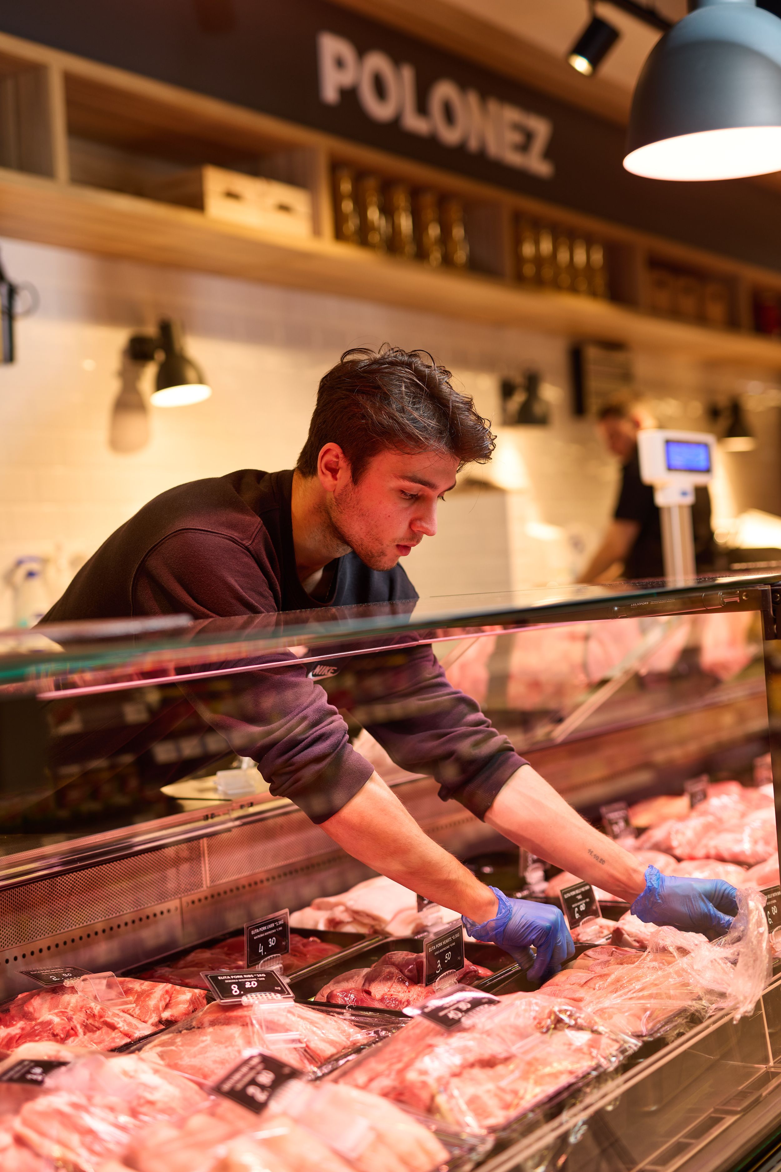 Butcher preparing meat at fresh meat counter display case.
