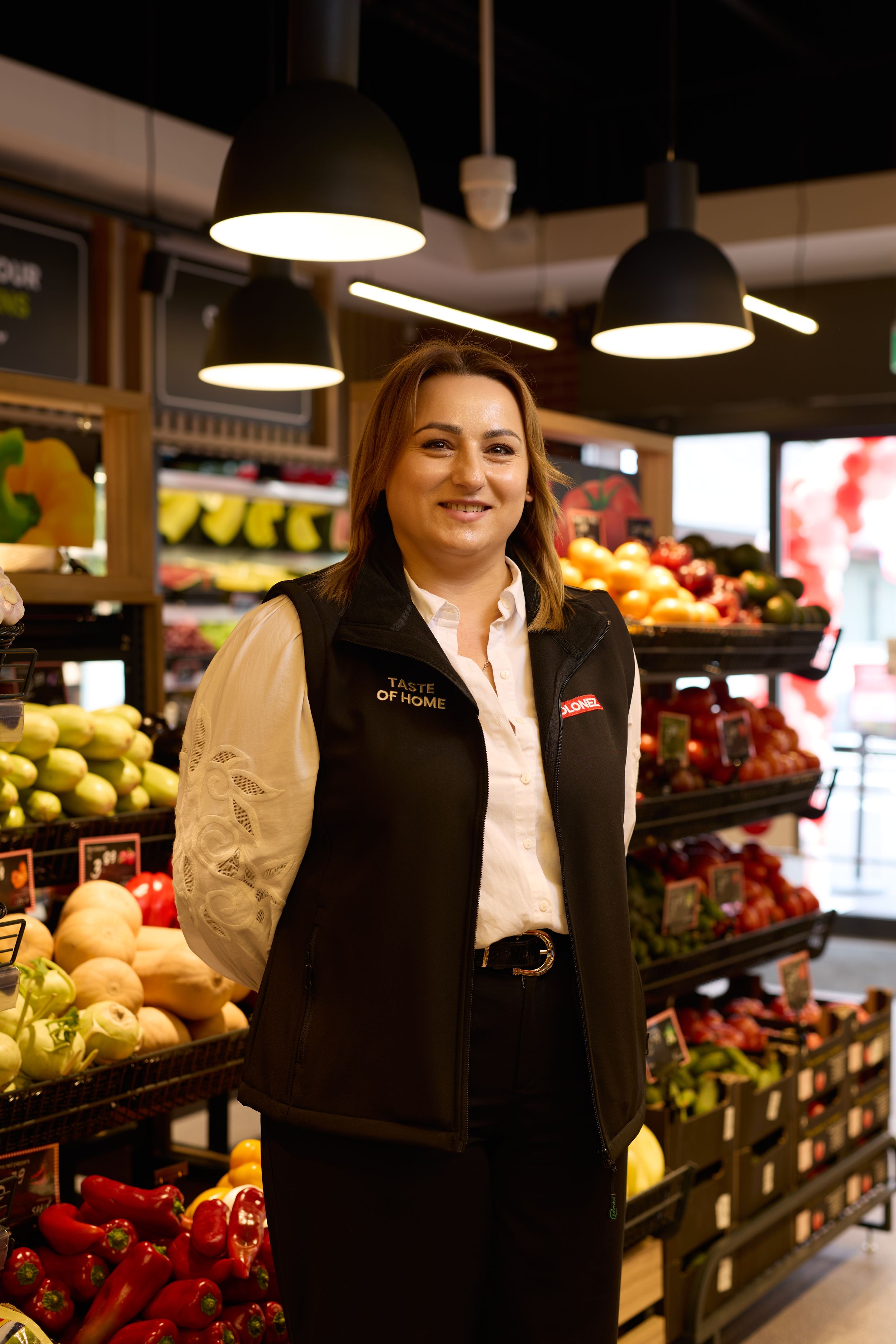 Staff member in black uniform standing in produce section of grocery store.