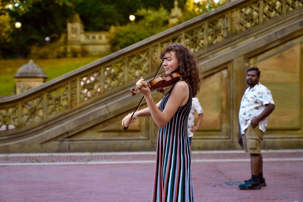 Musician in a striped dress performs with a flute on the steps of Bethesda Terrace in Central Park.