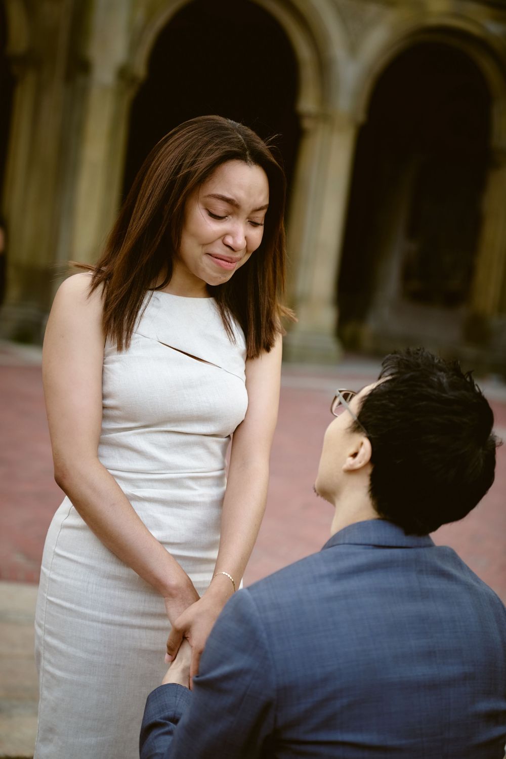 A couple shares a romantic proposal moment in an elegant arched corridor as they gaze at each other lovingly. Surprise engagement in central