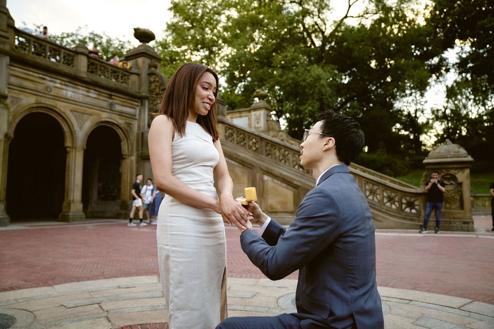A romantic proposal moment on grand stone steps at sunset with historic architecture in the background. Surprise engagement in central park