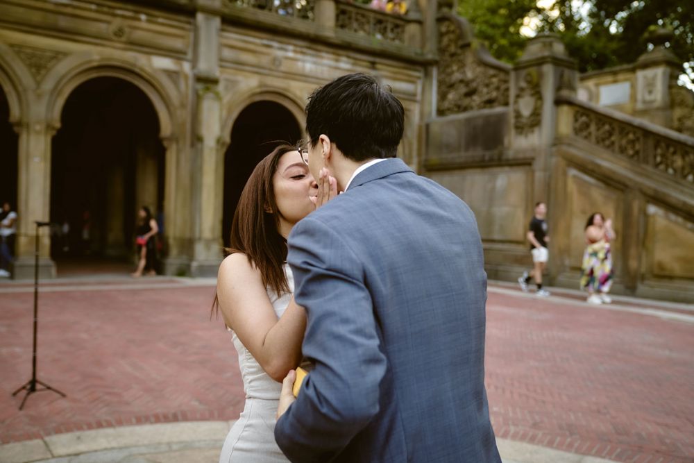 A couple shares a romantic kiss near an ornate stone staircase and archways at Bethesda Terrace in Central Park.