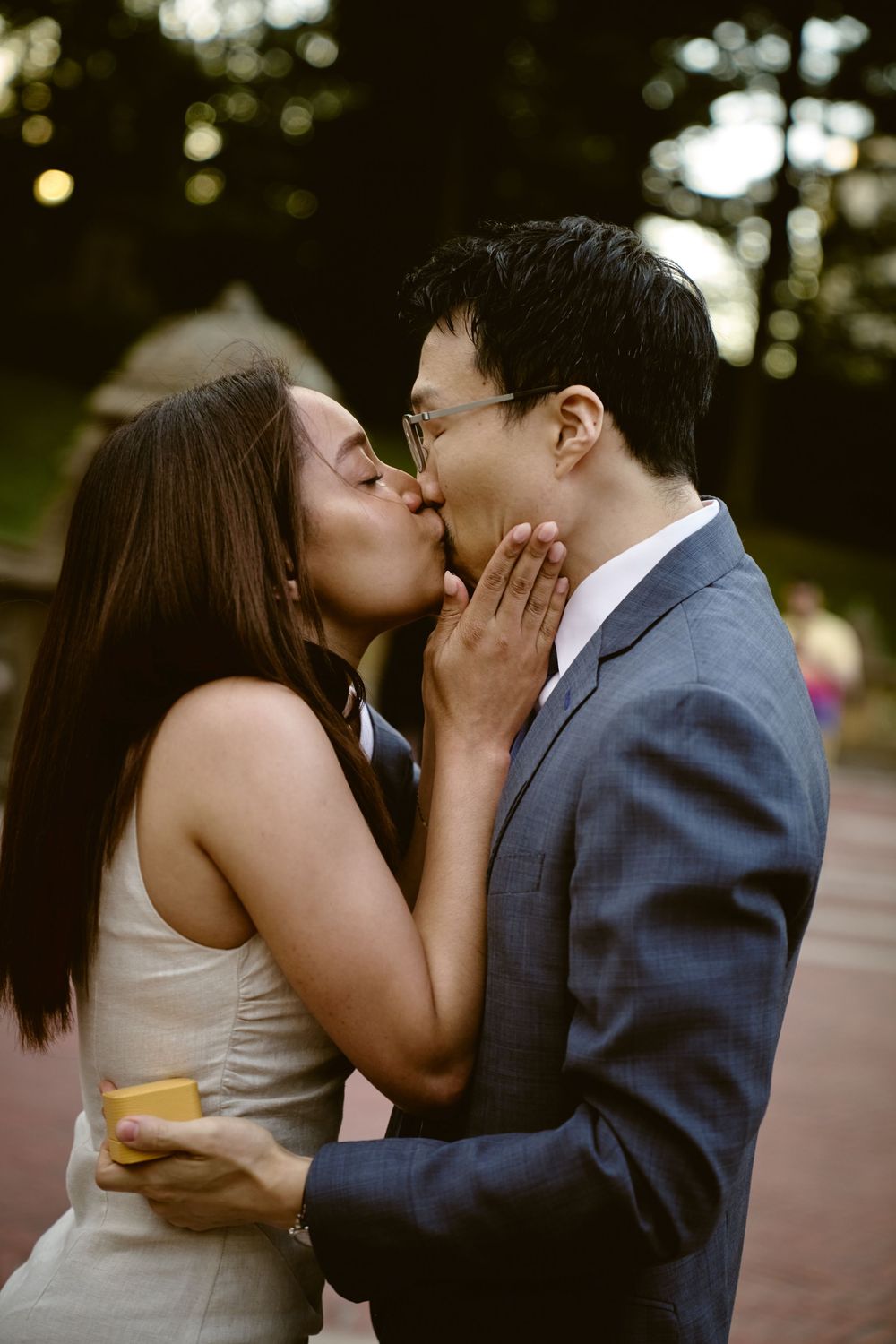 A couple shares a series of intimate kisses in a romantic outdoor setting during sunset. Surprise engagement in central park