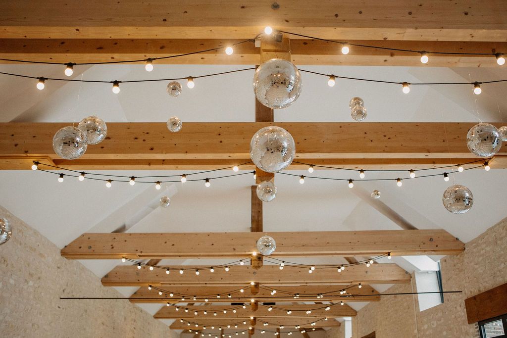 Rustic barn ceiling decorated with string lights and glass globe pendants on wooden beams.