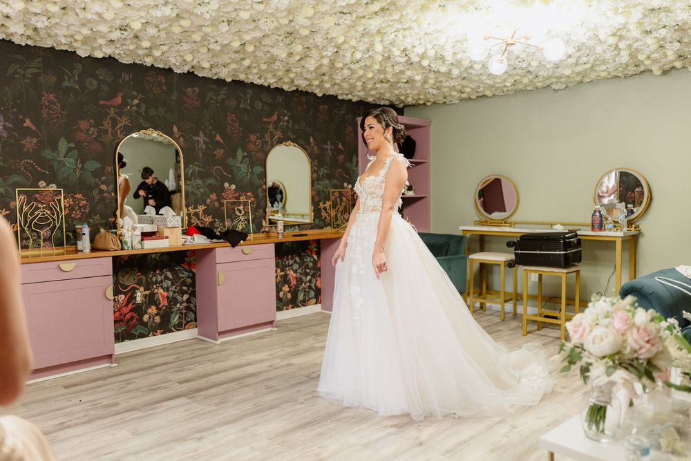 Wedding dress hanging in bridal preparation room with natural lighting.