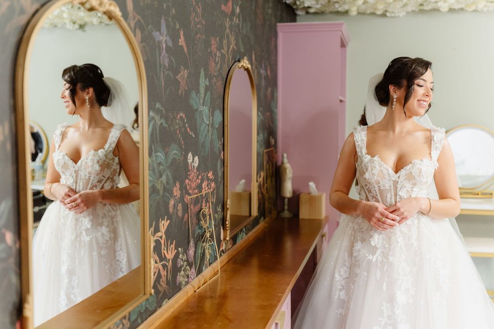 Series of elegant white wedding dresses displayed in boutique mirrors with vintage wallpaper backdrop.