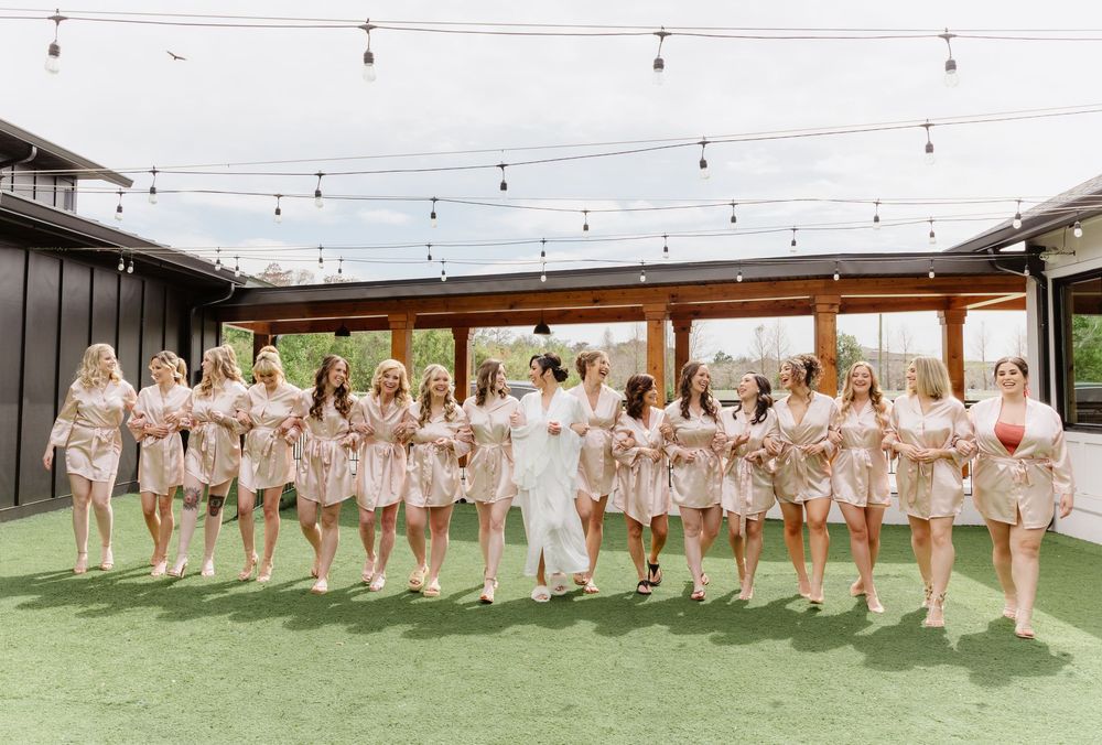 Wedding party in blush pink dresses standing in a line outdoors under string lights.