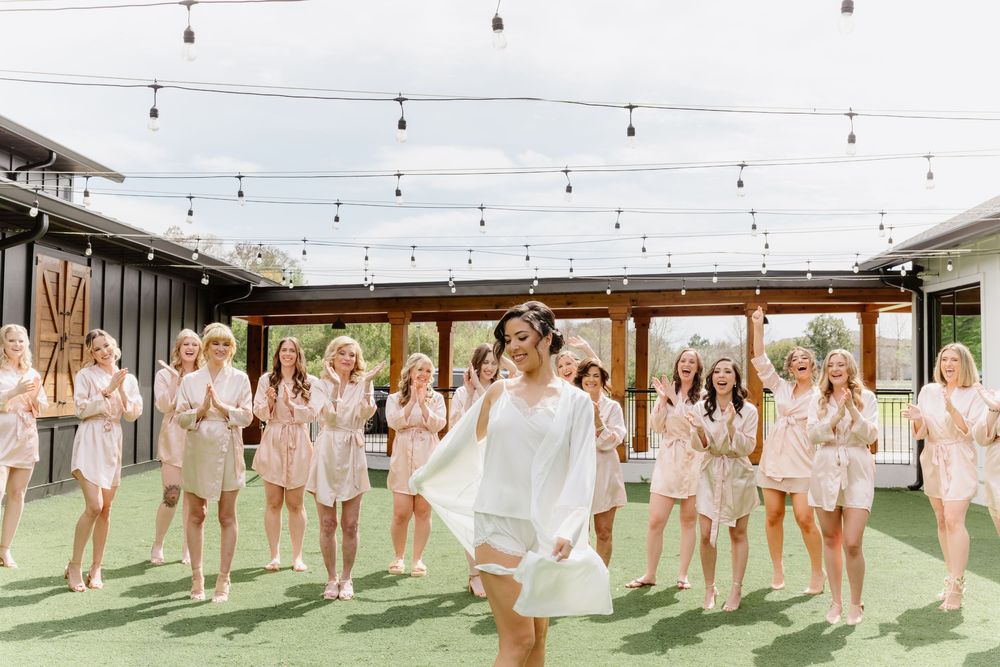 Wedding party poses outdoors under string lights in coordinated blush pink outfits.