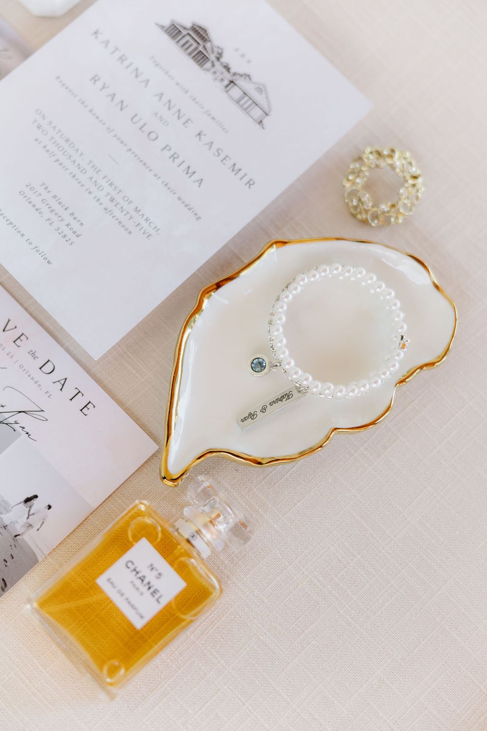 Wedding invitation details with perfume bottle and pearl accessories on white background.