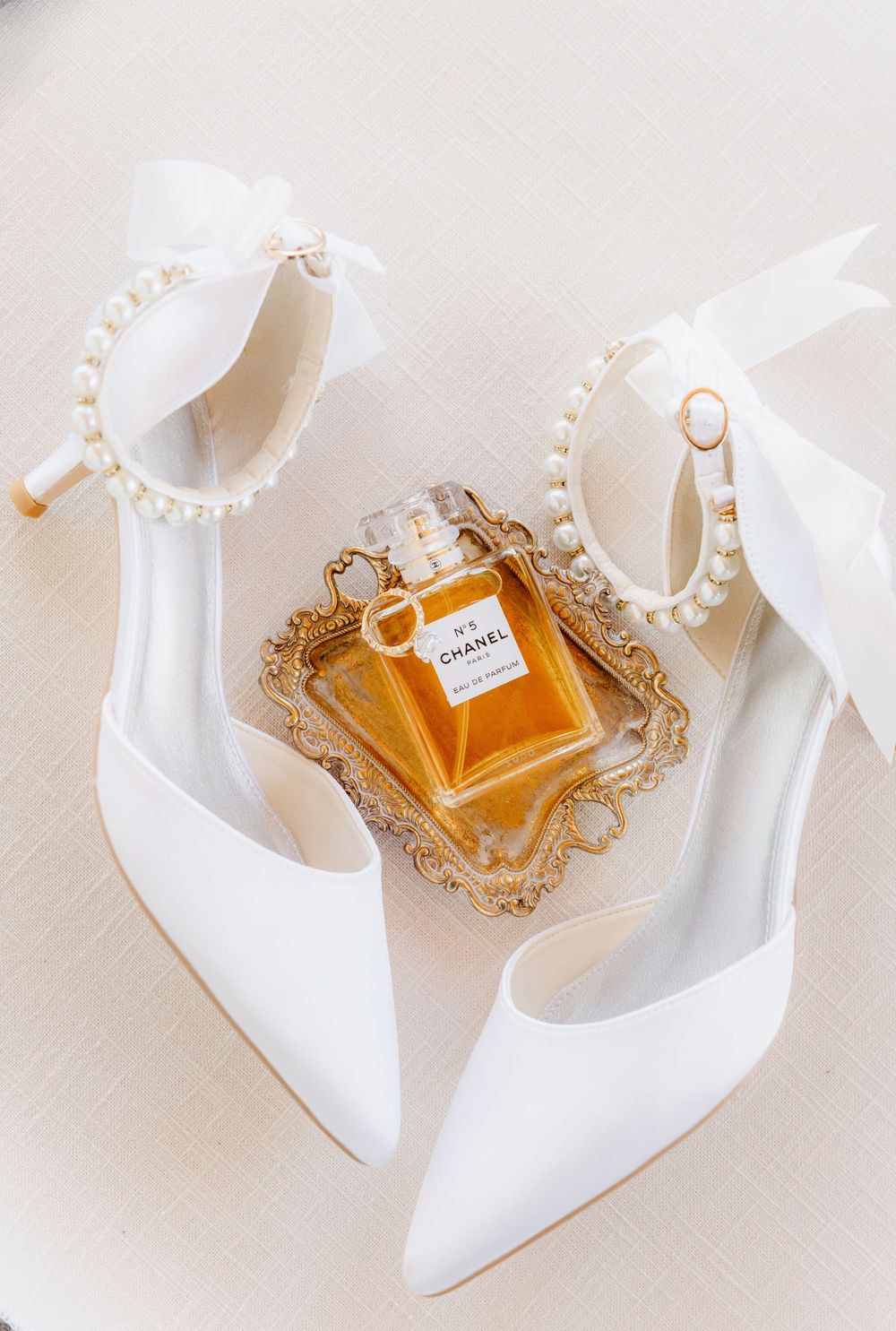 White bridal shoes and perfume bottle arranged on elegant gold-trimmed display.