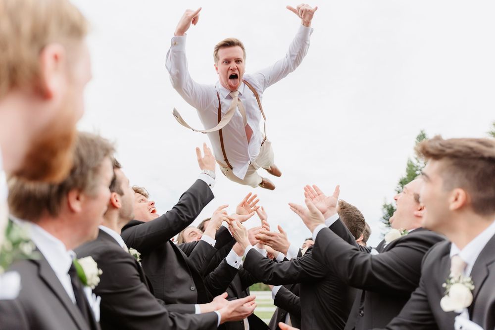 Groomsmen throwing the groom up in celebration outside during wedding festivities.