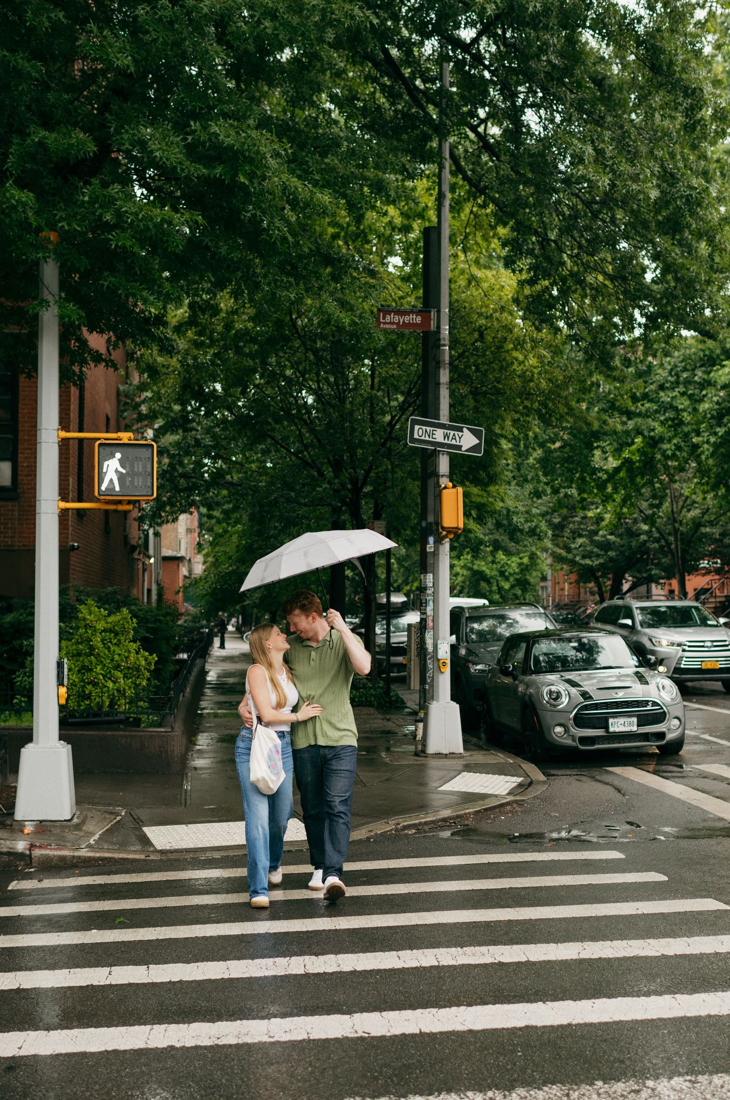 Couple walks together under a white umbrella across a crosswalk in an urban setting.
