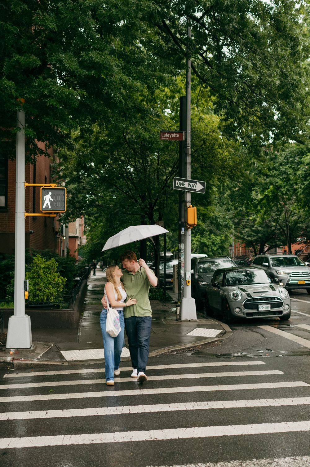 Couple walks together under a white umbrella across a crosswalk in an urban setting.
