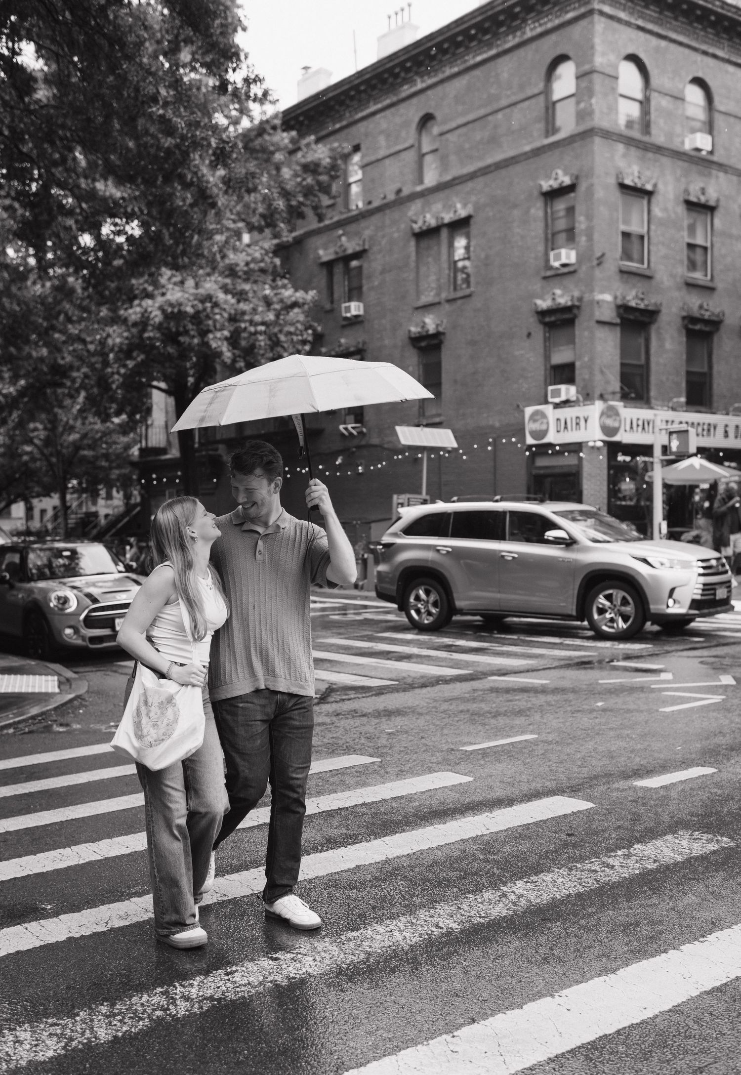 A couple shares an umbrella while crossing a city street on a rainy day.
