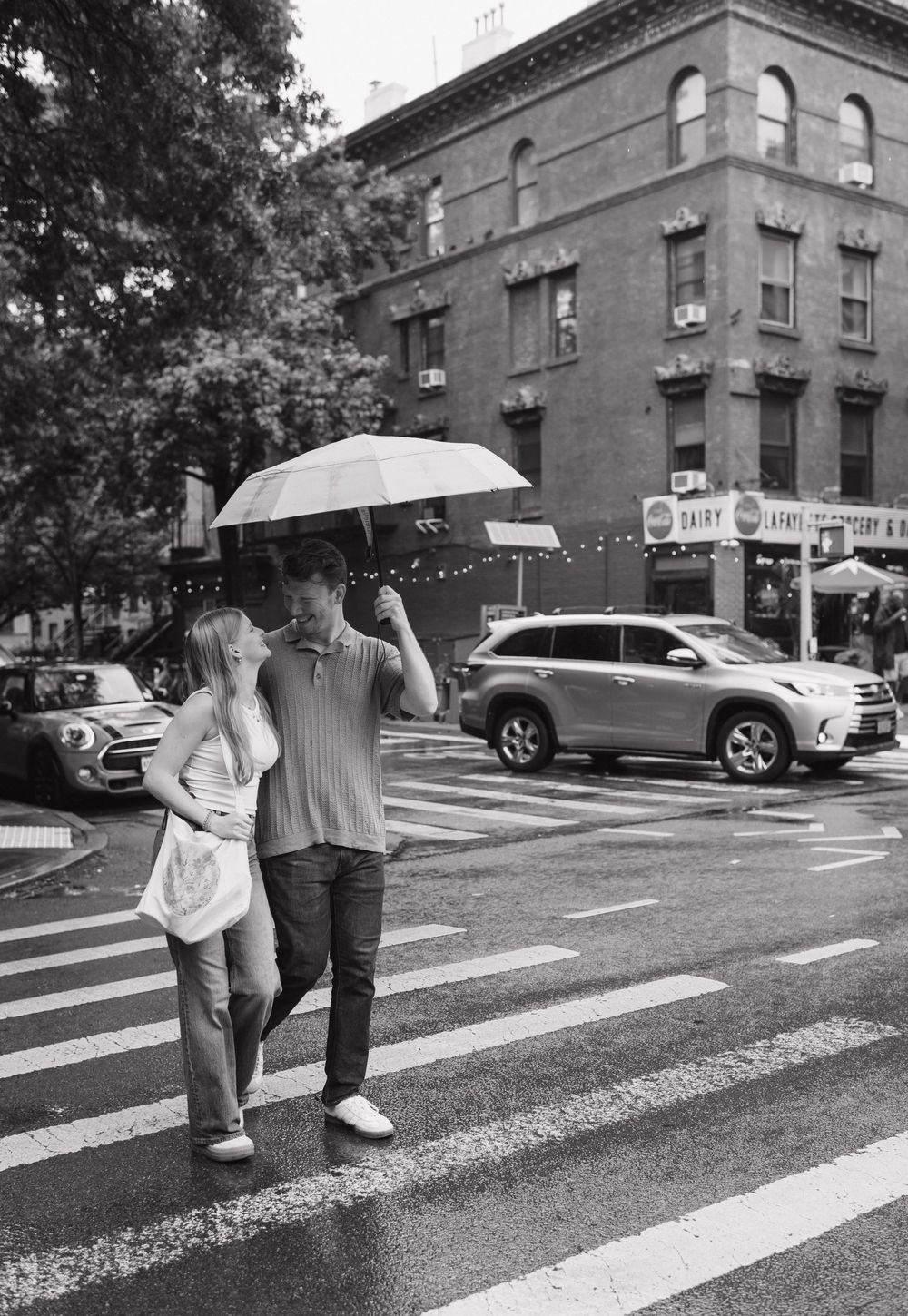 A couple shares an umbrella while crossing a city street on a rainy day.