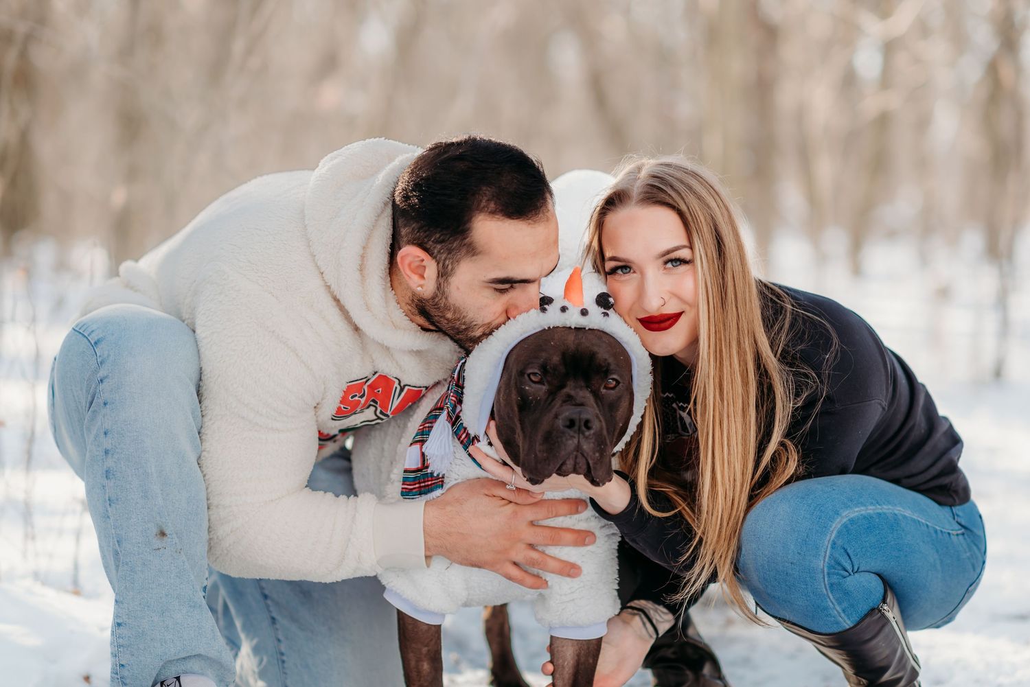 Happy couple with their cute grey French Bulldog enjoying a winter day in the snowy outdoors.