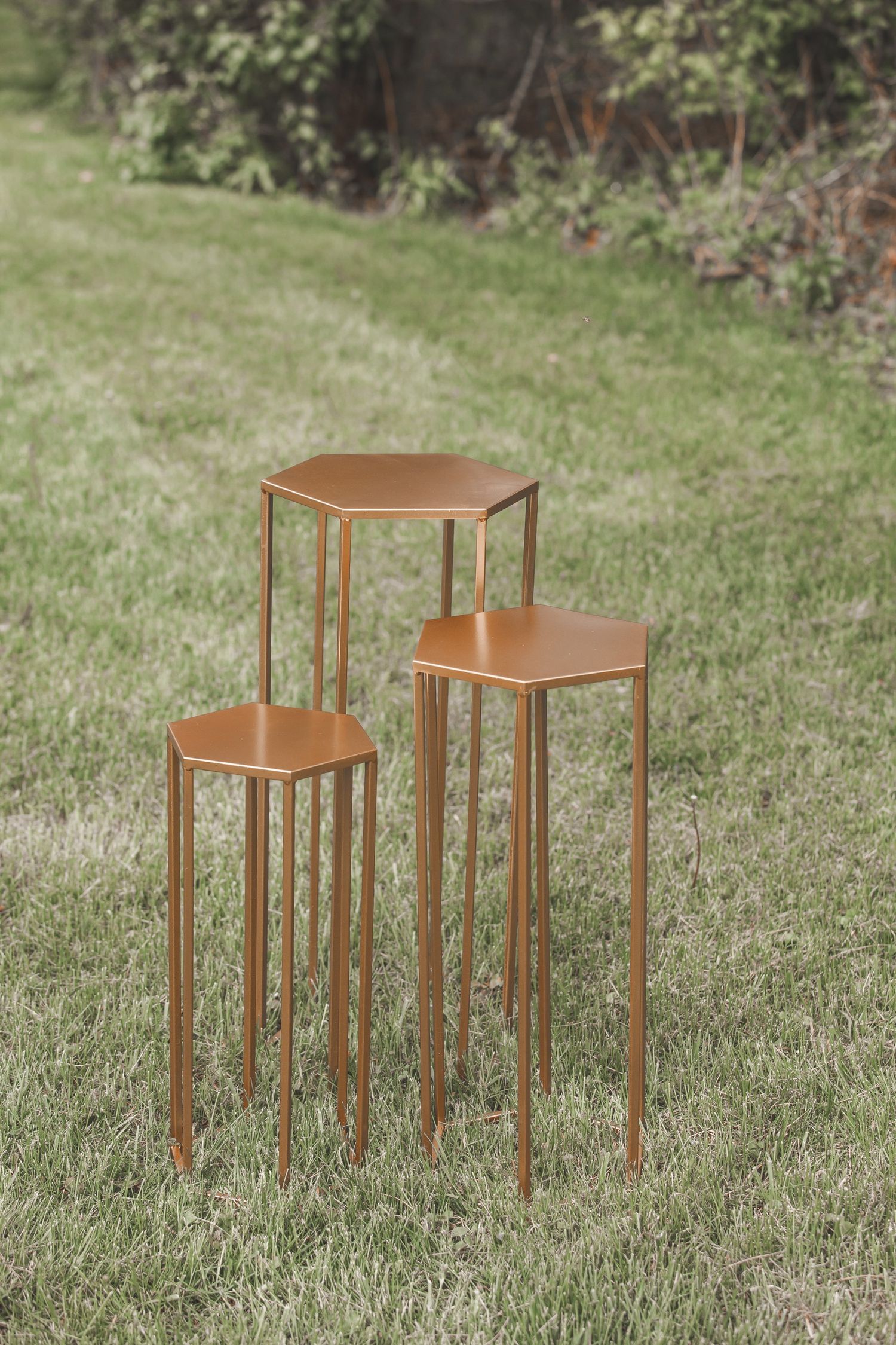 Three rustic copper-colored metal plant stands of varying heights displayed on green grass in a garden setting.