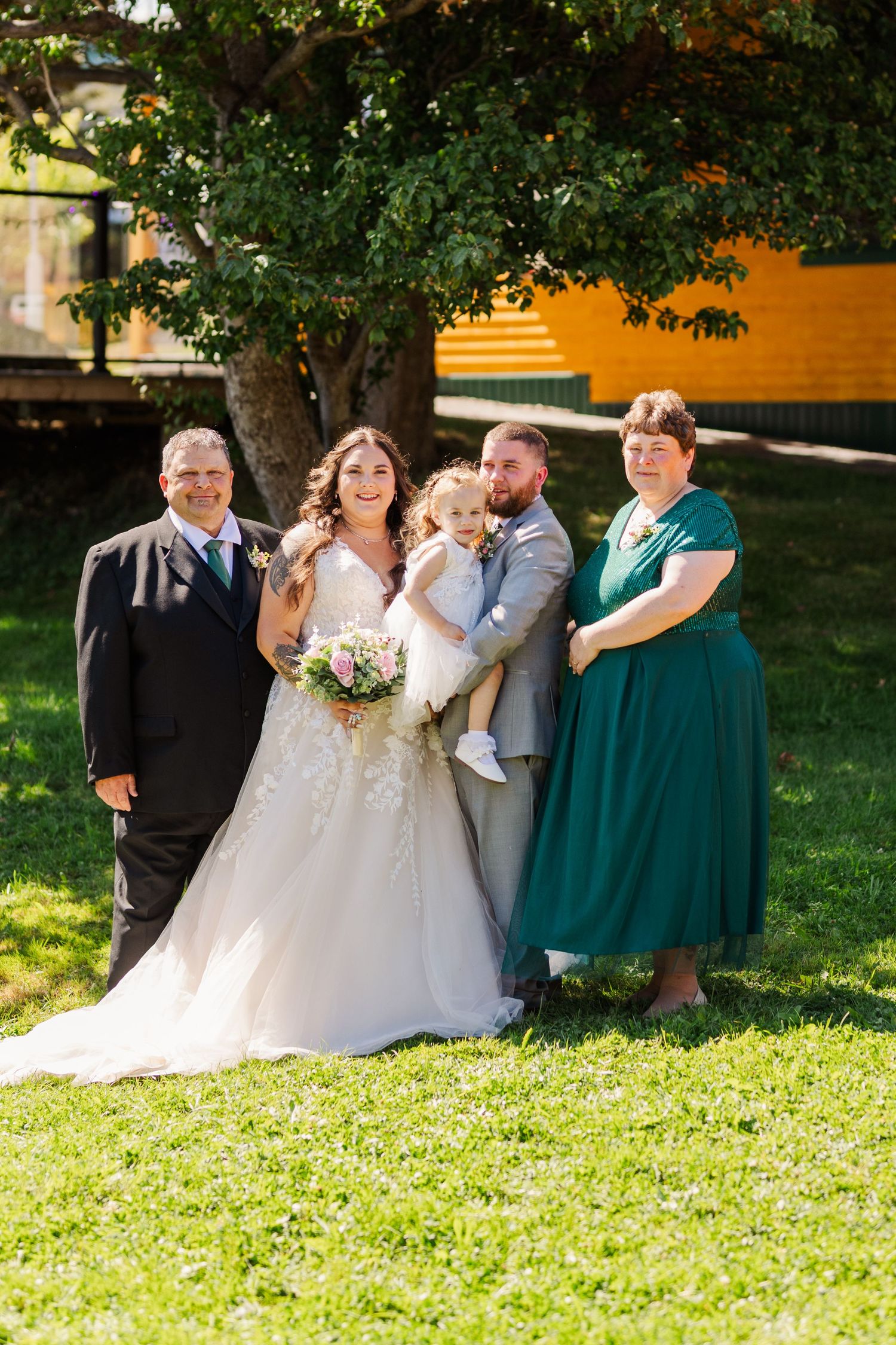 Wedding party in teal bridesmaid dresses and formal attire poses together on a sunny lawn for outdoor group photos.