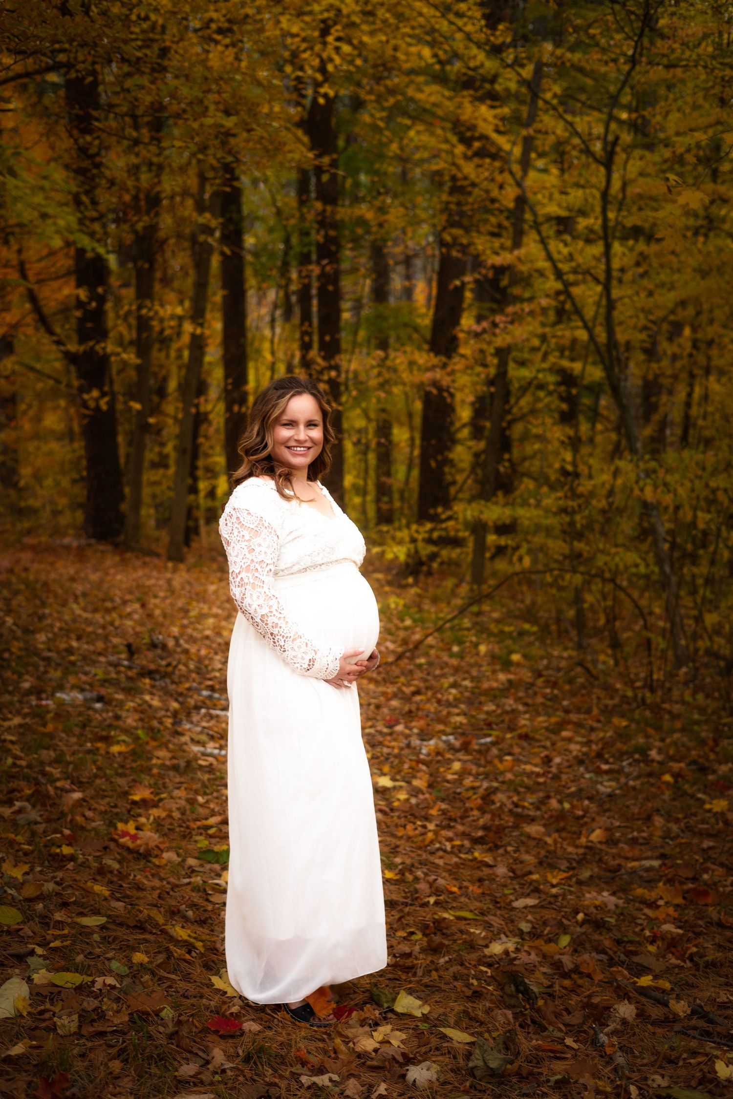 Person in white lace dress twirls during autumn woodland photoshoot with golden foliage in background.