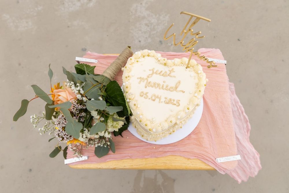 A white cake with pink sprinkles and decorative greenery sits on a blush pink tulle table runner.