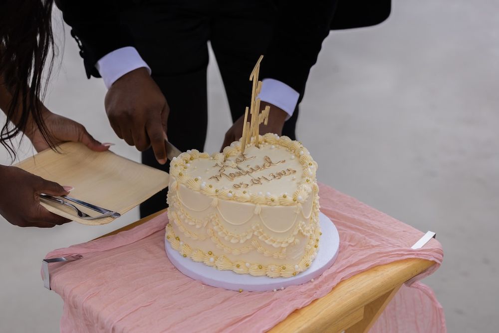 Hands cutting and serving slices of a white-frosted cake on a pink tablecloth.