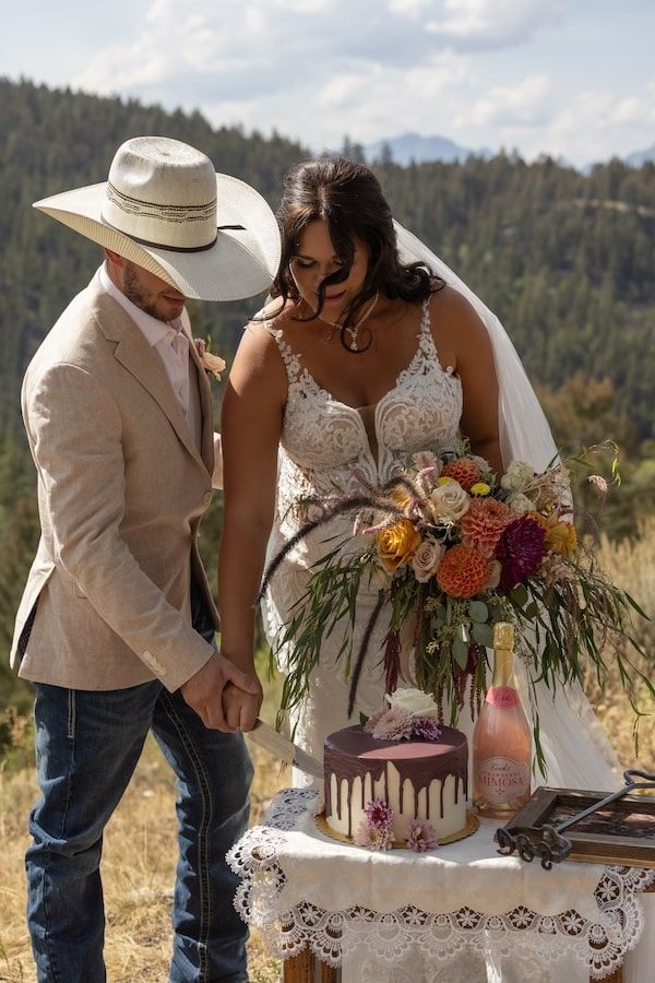 Newlywed couple sharing an intimate moment while cutting a pink ombre wedding cake in an outdoor mountain setting.