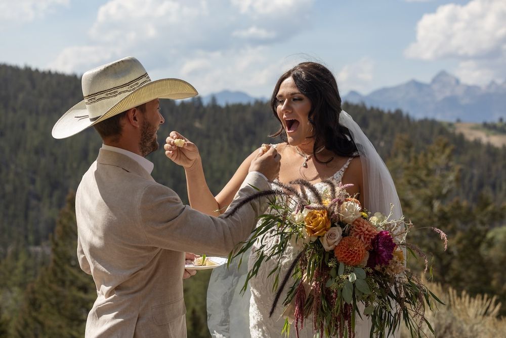A wedding couple and officiant celebrate during an outdoor mountain ceremony with vibrant fall flowers.