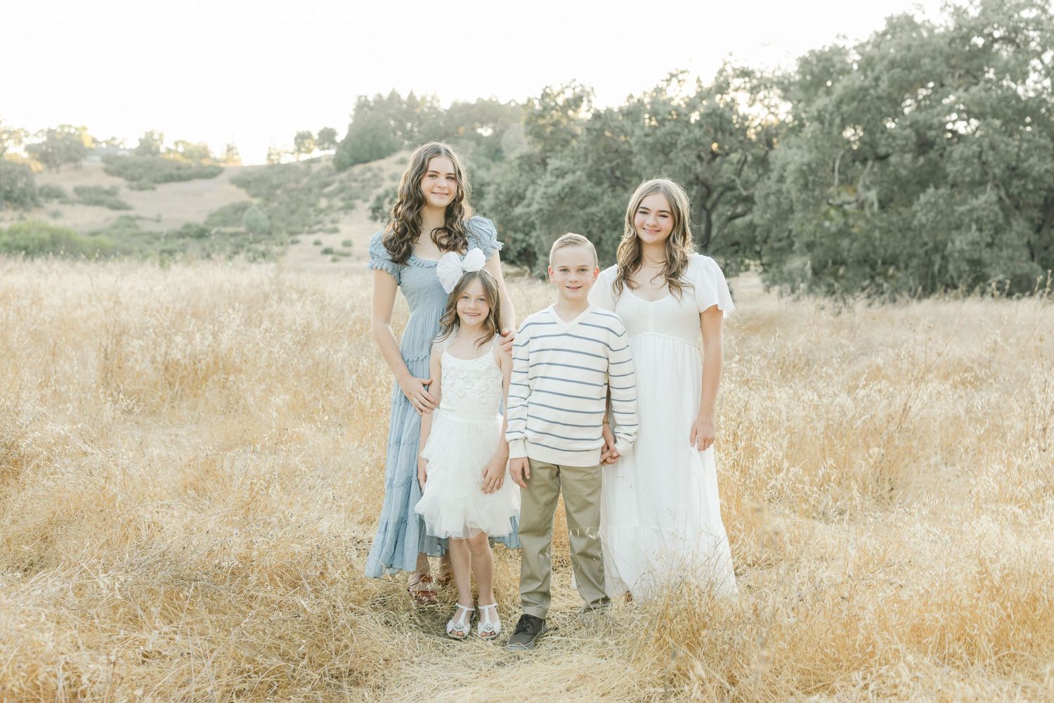 A family walks through a golden field during sunset while wearing coordinated neutral-toned outfits captured by Chelsee Rawe Photography.