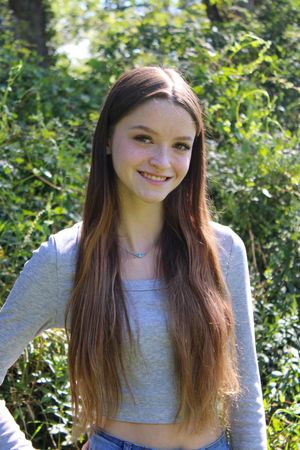 Person wearing grey long sleeve top poses in sunny outdoor garden setting.