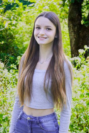 Person in crop top and denim poses in wooded area with sunlit foliage.