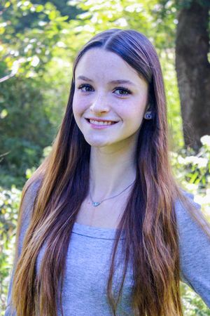 Person in grey top poses against natural greenery in outdoor portrait series.