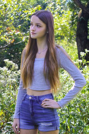 Person in casual grey top and denim shorts poses against flowering garden background.